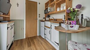 A compact kitchen with a microwave, refrigerator, wooden shelves, and a small table with a vase of flowers. - 1 Bed in Penrith (oc-85532) (Deepdale)