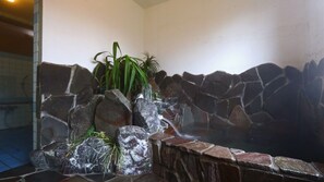 A hot spring area with a rocky wall, a small waterfall, and some greenery. - Guesthouse Shinkoen (Nikko)