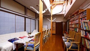 A room with a dining table, chairs, a bookshelf, and a traditional Japanese sliding door. - Guesthouse Shinkoen (Nikko)