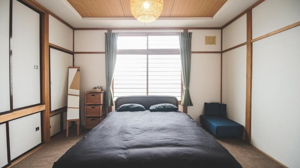 A traditional Japanese-style bedroom with tatami flooring, a low wooden bed, a desk with a lamp, and a sliding door.