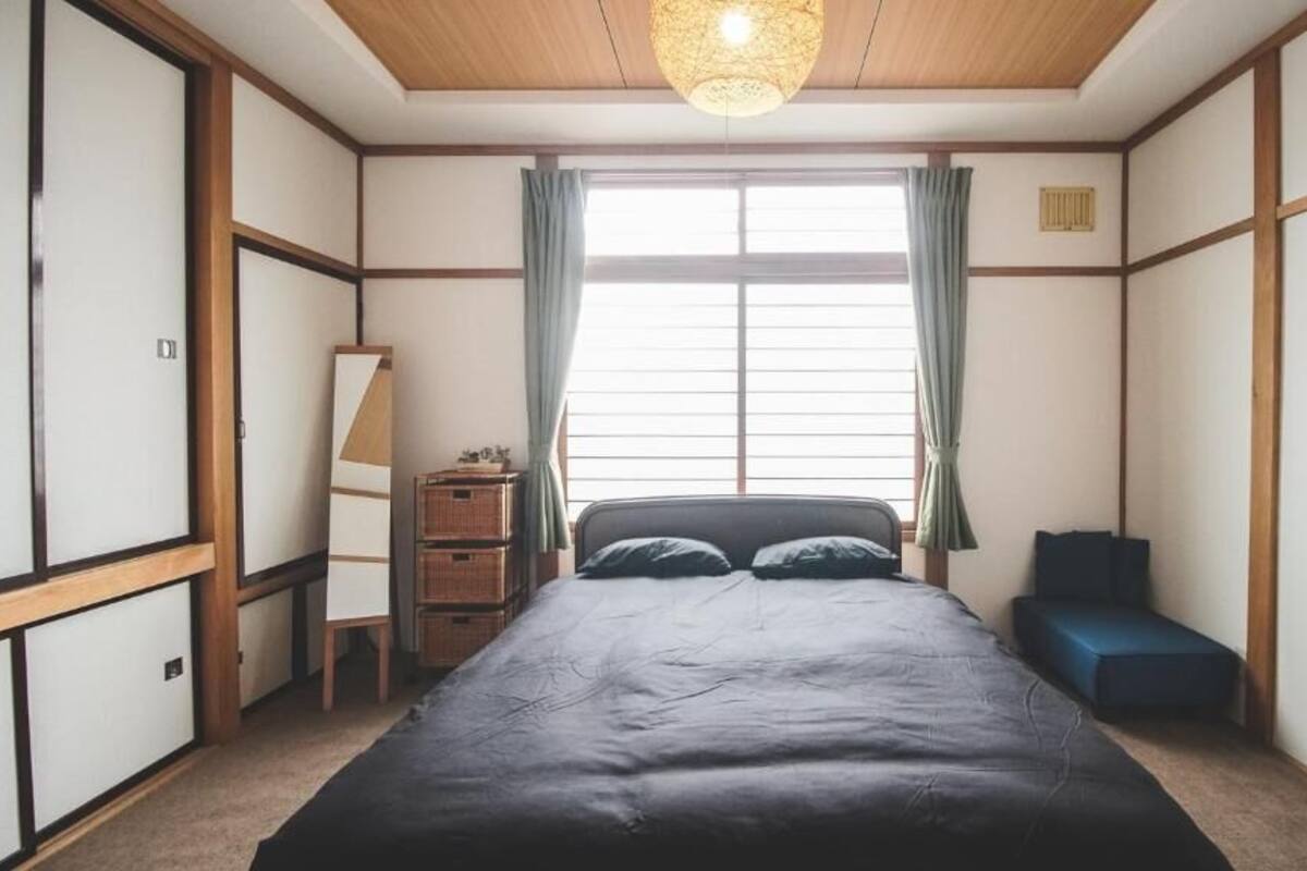 Ein traditionelles japanisches Schlafzimmer mit Tatami-Böden, einem niedrigen hölzernen Bett, einem Schreibtisch mit Lampe und einer Schiebetür.