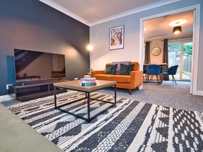 A modern living room with a sofa, coffee table, and a fireplace. There is a dining area with chairs and a table visible through an open door. - *Sleeps 6* 4 Bedroom House + DriveContractors (Birmingham)