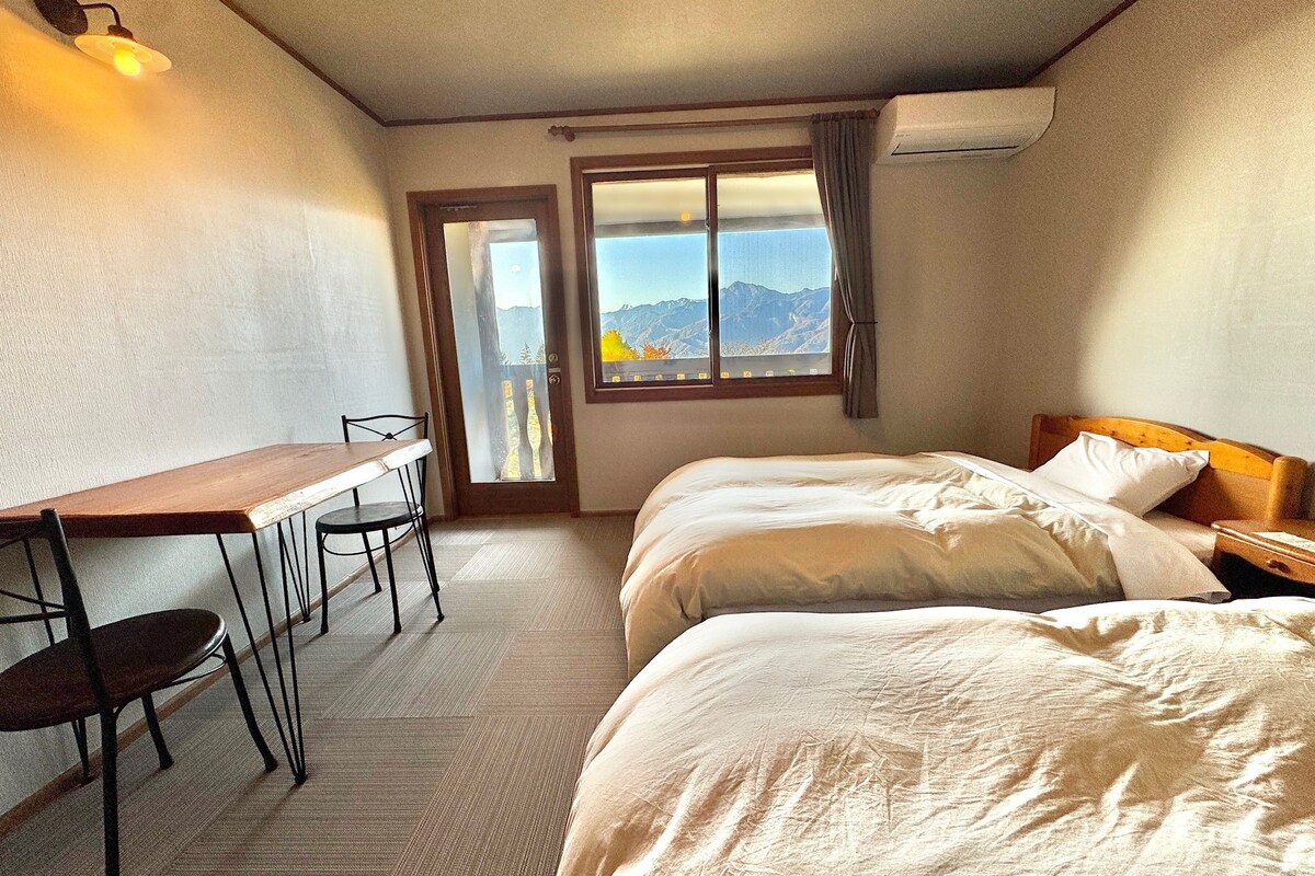 A hotel room with a bed, a desk, and a chair. There is a window with a mountain view.