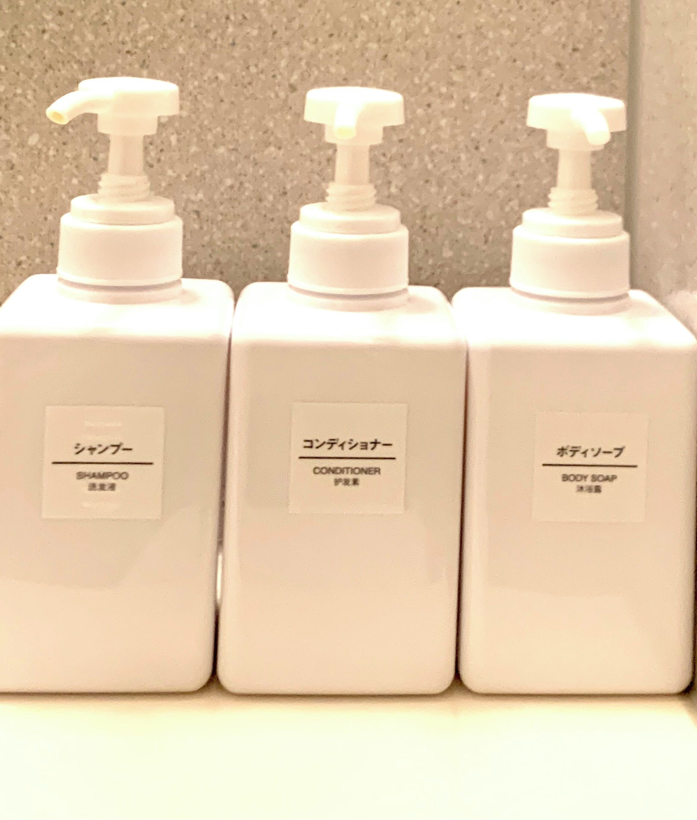Trois flacons blancs dotés de pompes doseuses, étiquetés « shampoing », « après-shampoing » et « savon pour le corps ».
