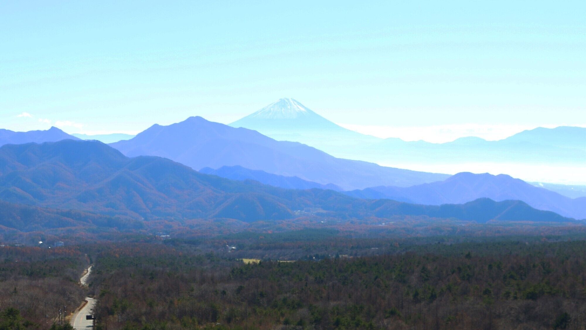 Paisagem montanhosa com um pico imponente, vales arborizados e uma estrada.