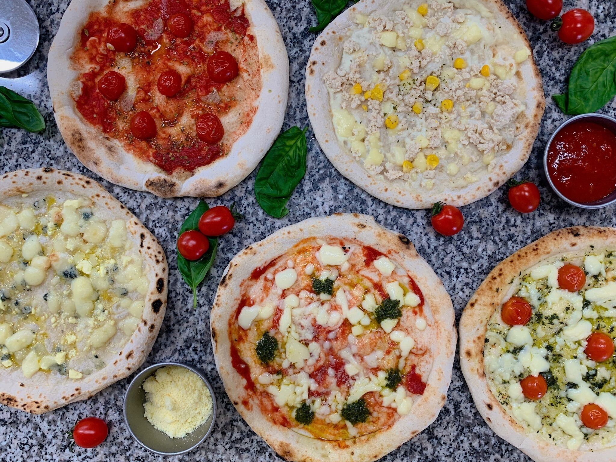 Six pizzas with various toppings on a granite countertop.