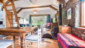 A rustic interior with exposed wooden beams, a stone wall, a fireplace, and a view of the outdoors. - 1 Bed in Llandysul (oc-85671) (Capel Dewi)