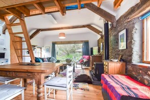 Ein rustikales Interieur mit freiliegenden Holzbalken, einer Steinwand, einem Kamin und Blick ins Freie.