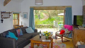 A cozy living room with a sofa, a wooden coffee table, and a rocking chair. There is a television on a wooden cabinet, and a window with curtains. - 1 Bed in Llandysul (oc-85671) (Capel Dewi)