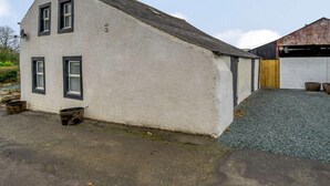 A single-story building with a sloped roof, a small porch area, and a gravel driveway. - 2 Bed in Cockermouth (oc-85680) (Blindcrake)