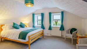 A bedroom with a bed, a chair, a table, a window with curtains, a radiator, and a hanging light fixture. - 2 Bed in Cockermouth (oc-85680) (Blindcrake)