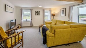 A living room with a yellow sofa, wooden chair, television, and windows. - 2 Bed in Cockermouth (oc-85680) (Blindcrake)