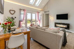 Ein modernes Wohnzimmer mit einer Couch, einem Esstisch mit Stühlen, einem Flachbildfernseher und einem Kamin.