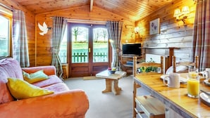 A cozy cabin interior with a wooden ceiling, a sofa with cushions, a dining table with a coffee setup, and a TV. - 2 Bed in Honiton (oc-85816) (Sheldon)