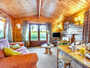 A cozy cabin interior with a wooden ceiling, a sofa with cushions, a dining table with a coffee setup, and a TV. - 2 Bed in Honiton (oc-85816) (Sheldon)