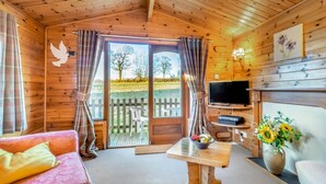 A wooden cabin interior with a sofa, a table with a bowl, a TV, and a flower vase. - 2 Bed in Honiton (oc-85816) (Sheldon)