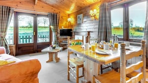 A wooden cabin interior with a dining area, a television, and a view of the outdoors. - 2 Bed in Honiton (oc-85816) (Sheldon)