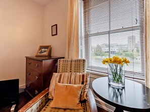 A room with a chair, a small table with a vase of flowers, a wooden dresser, and a window with blinds. - 4 Bed in Pembroke (oc-85835) (Pembroke)