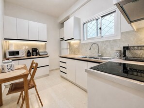 Eine moderne Küche mit weißen Schränken, einer schwarzen Induktionskochplatte, einer Spüle aus Edelstahl und einem Fenster mit Rautenmuster-Glas.