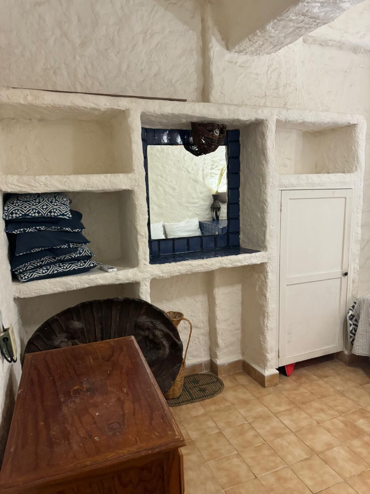 Une pièce rustique avec une table en bois, une armoire blanche et une étagère ornée de coussins à motifs.