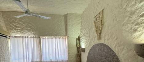 Un dormitorio con cama, ventilador de techo, lámpara de pared y ventana con cortinas.