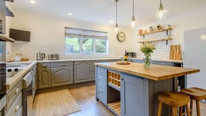 Een moderne keuken met een centraal eiland, houten krukken, een klok en een raam met uitzicht.