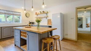 Een keuken met een centraal eiland, barkrukken, hangende hanglampen en een koelkast.