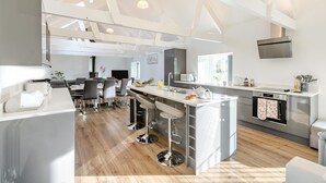 Uma cozinha moderna com uma ilha central, banquetas, área de refeições com cadeiras e uma grande janela que oferece iluminação natural.