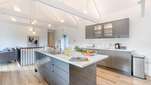 Cozinha moderna com ilha central, eletrodomésticos de aço inoxidável e área de jantar com sofá cinza.