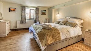Ein Schlafzimmer mit einem Bett, Nachttischen, einem Fenster mit Vorhängen, einer Heizung und einem Bild an der Wand.