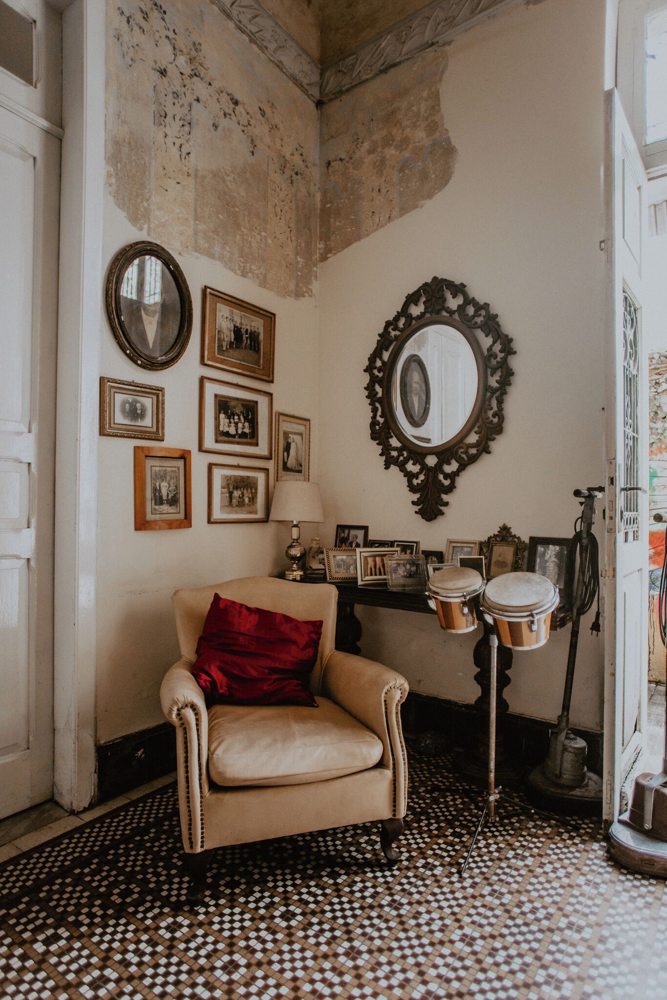 Una habitació amb un paviment estampat, una cadira amb coixí vermell i una paret decorada amb quadres i miralls.