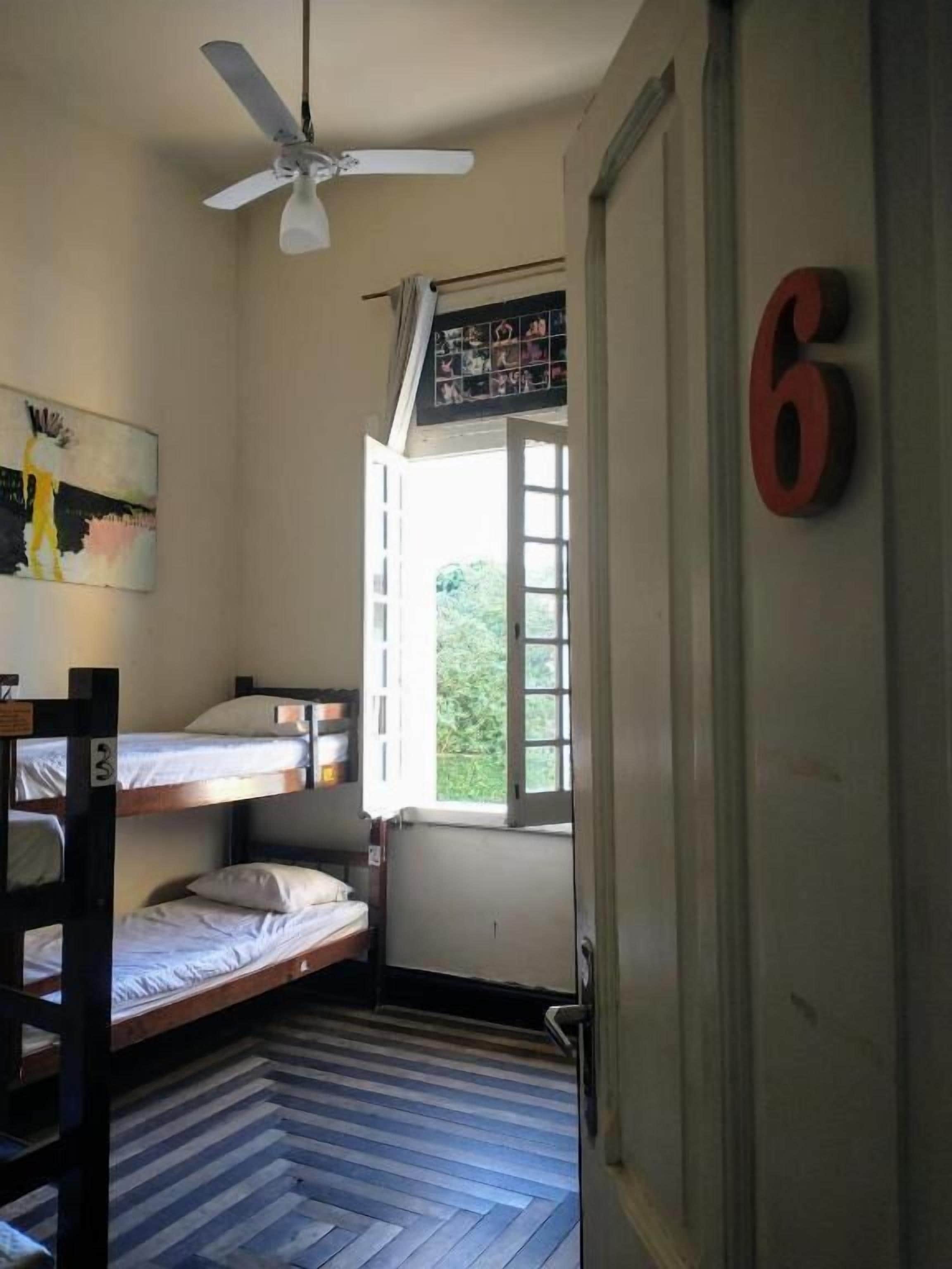 A room with bunk beds, a ceiling fan, a window with a view, and a door marked with the number 6.
