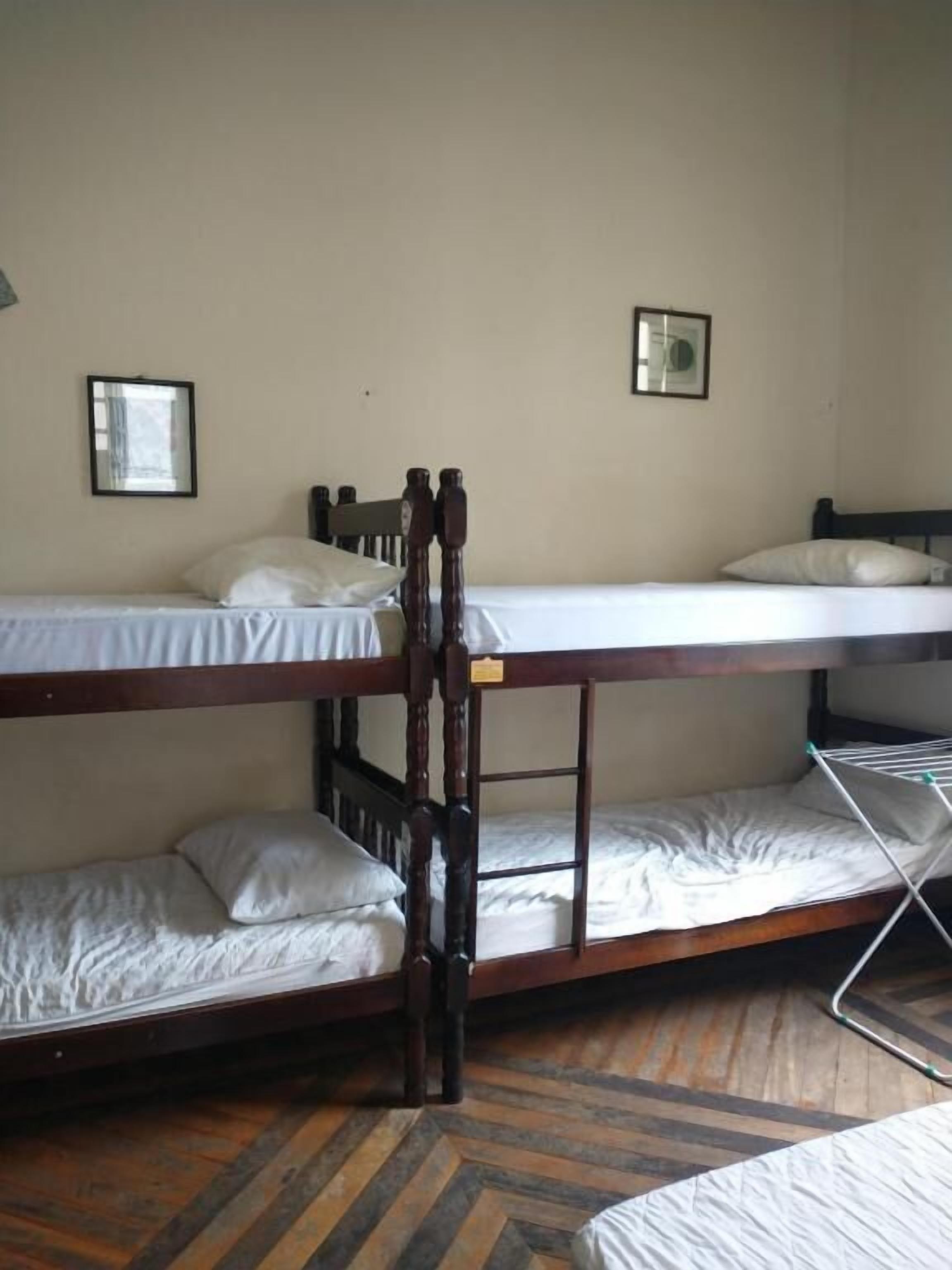 Quarto com beliche, dois colchões, piso de madeira e duas imagens emolduradas na parede.