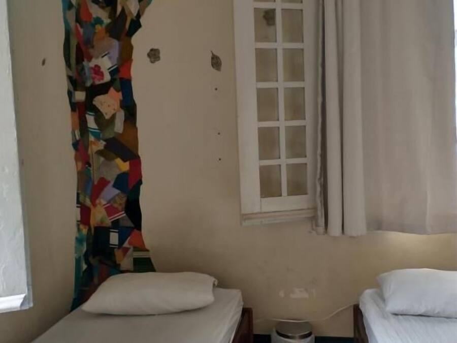 A small, single-room accommodation with a bed, a window with curtains, and a wall mural.
