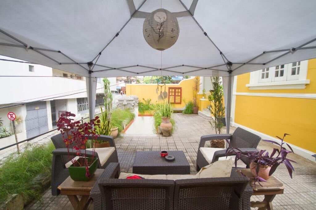 Un patio al aire libre con mobiliario de mimbre, plantas en macetas y un reloj en el techo.