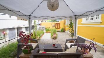 Un patio al aire libre con mobiliario de mimbre, plantas en macetas y un reloj en el techo.