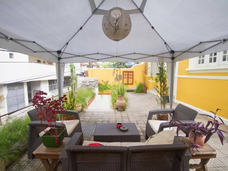 Un patio al aire libre con mobiliario de mimbre, plantas en macetas y un reloj en el techo.