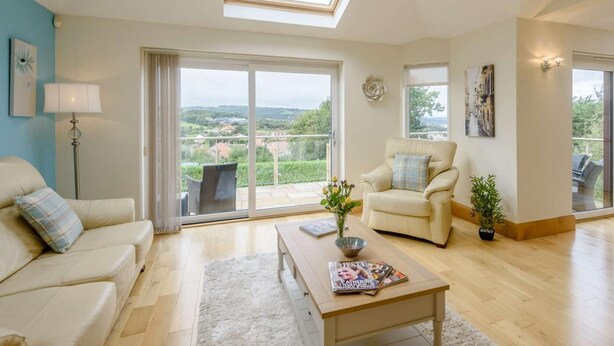 A spacious living room with a high ceiling, a skylight, a large sliding glass door leading to a balcony, and a view of the countryside. - 3 Bed in Colwyn Bay (oc-85763) (Hen Golwyn)