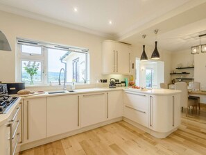 A modern kitchen with white cabinetry, a built-in stove, and a large window. - 3 Bed in Colwyn Bay (oc-85763) (Hen Golwyn)