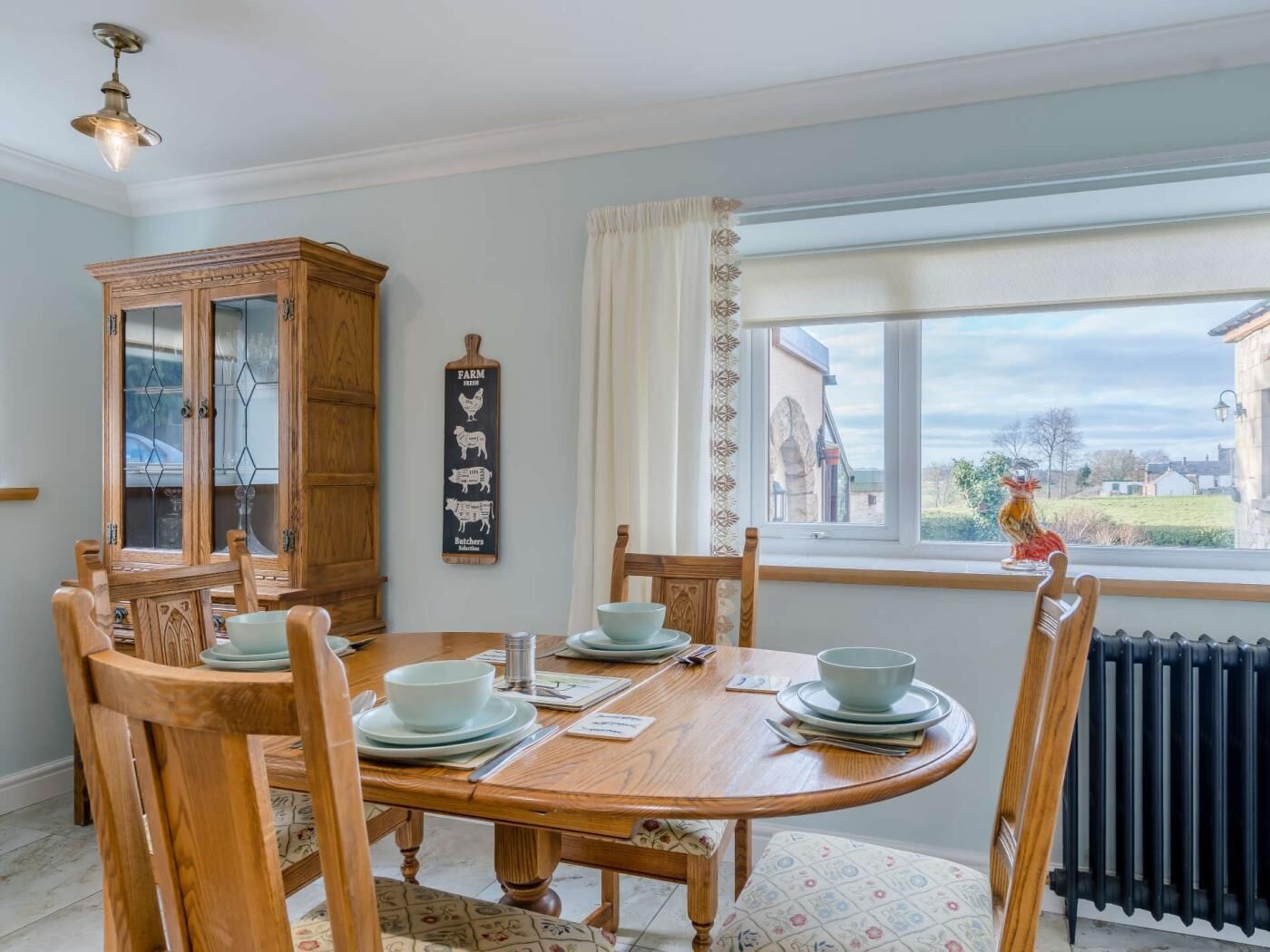 Une salle à manger avec une table en bois, des chaises, un buffet et une fenêtre donnant sur un beau paysage.