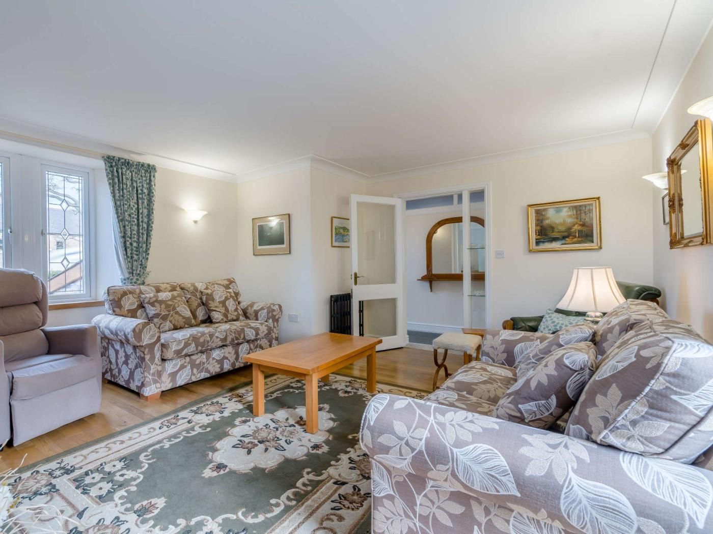 Un salon comprenant un canapé, un fauteuil et une table basse. Une porte donne accès à une autre pièce, et un tableau est accroché au mur.