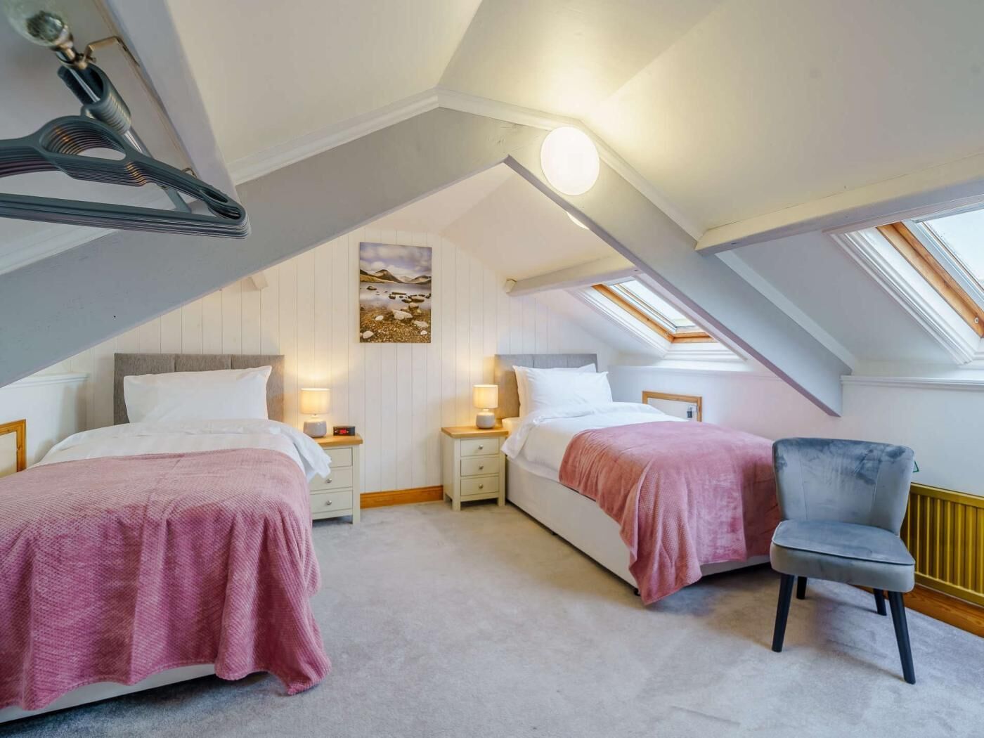 A bedroom with two beds, a chair, and a skylight.