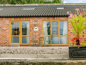 A brick building with two windows, a small table with chairs, and a flower pot. - 1 Bed in Ripon (oc-85511) (Masham)