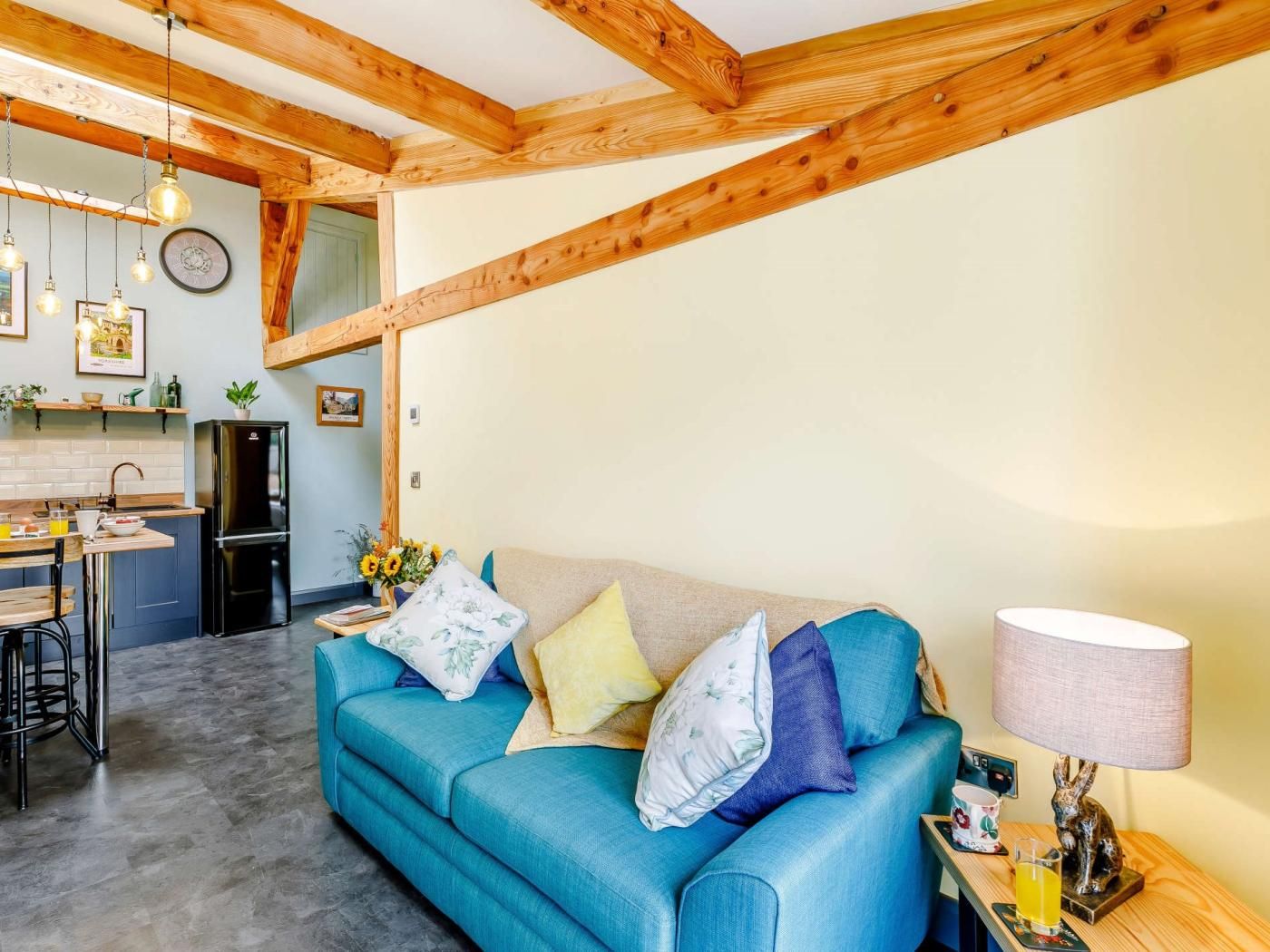 A cozy living room with a blue sofa, a kitchen area with a refrigerator, and a dining space with chairs.