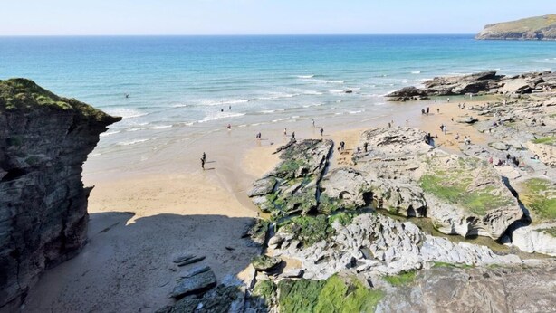 Ein Küstenstrand mit felsigem Gelände und klarem, blauem Wasser.