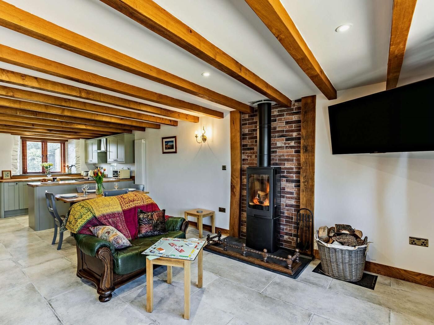 A cozy living room with a fireplace, wooden beams, a sofa, a coffee table, and a TV mounted on the wall.