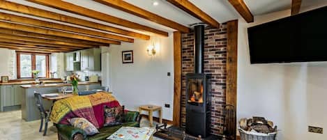 A cozy living room with a fireplace, wooden beams, a sofa, a coffee table, and a TV mounted on the wall.