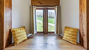 Ein Eckzimmer mit einer Holzbank, zwei Kissen und Blick auf eine grüne Landschaft durch eine Glastür.