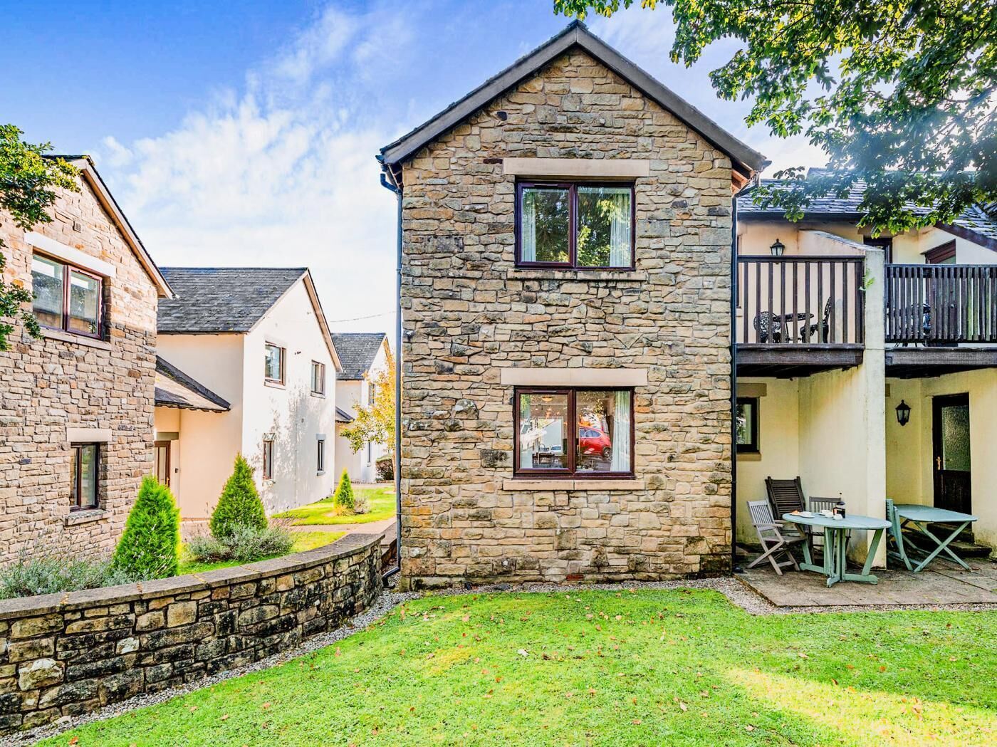 A two-story stone house with a balcony, a small garden, and a patio with outdoor furniture.