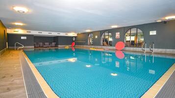 An indoor swimming pool with clear water, safety signs, and a tiled floor.